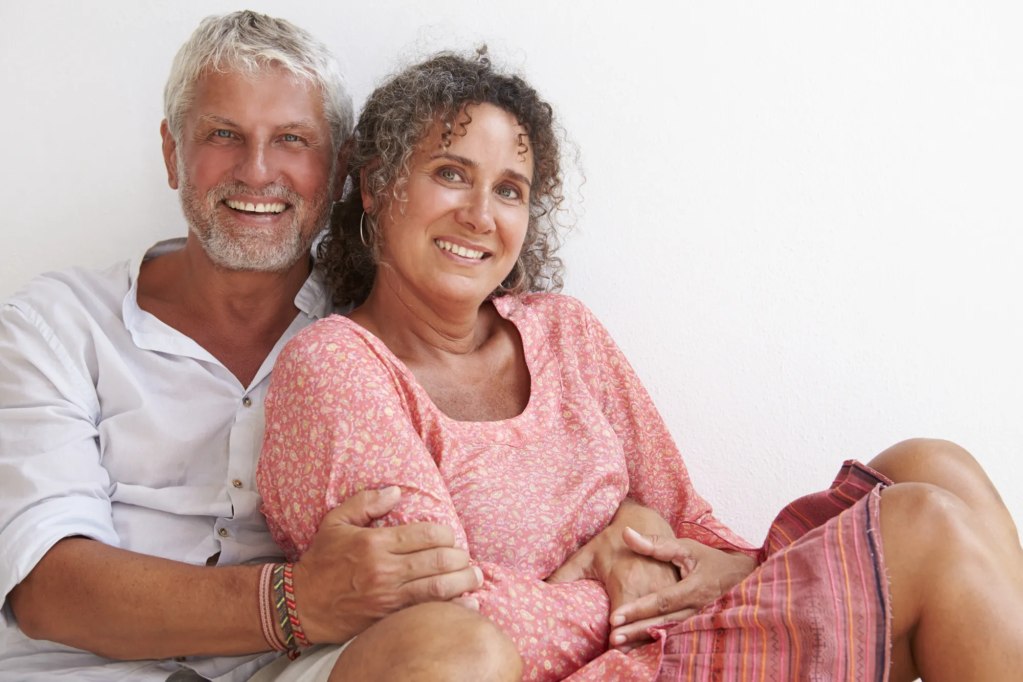 Smiling couple sitting together against a white background.
