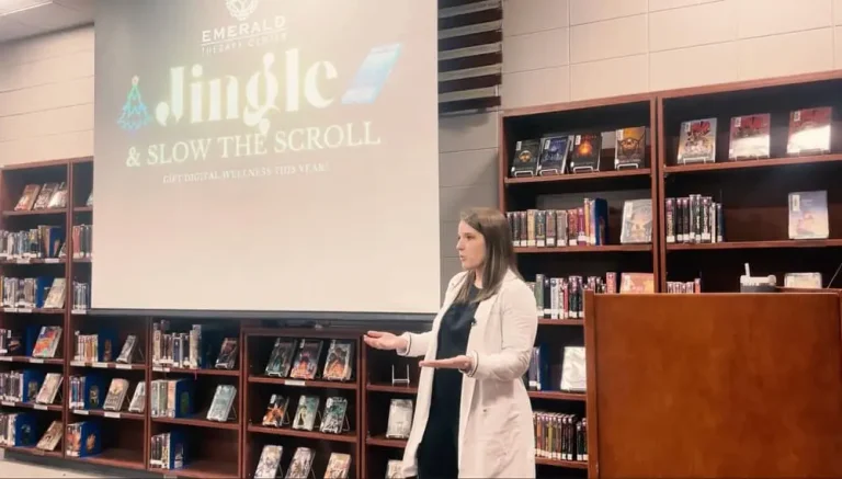 A woman presents in front of a screen displaying "Jingle & Slow the Scroll" in a library setting.