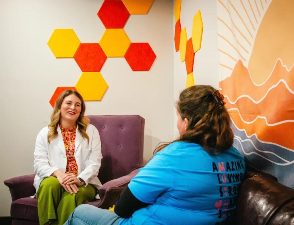 Two women talking in a room with colorful hexagon and landscape wall art.