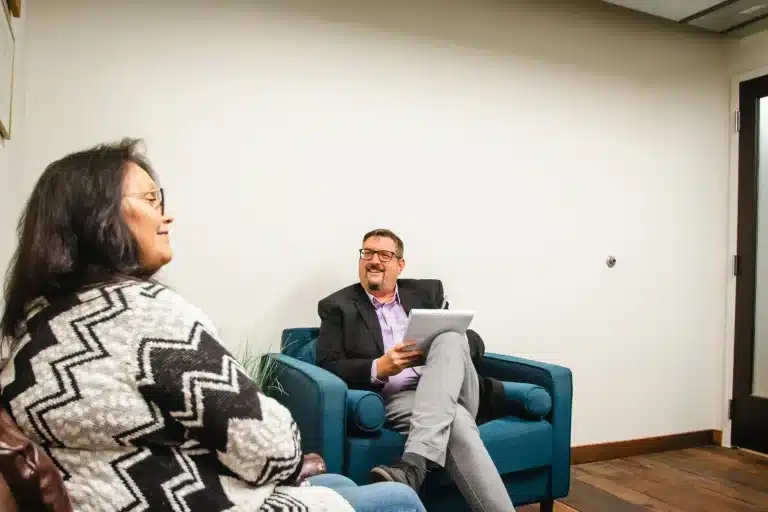 A man and woman are seated in a room, talking and smiling.