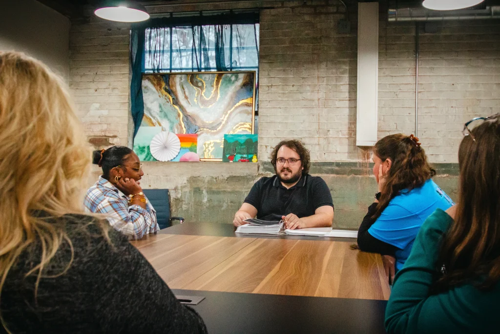A group of five people engaged in a meeting around a conference table.
