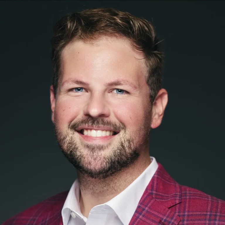 Smiling man in a red plaid suit against a dark background.