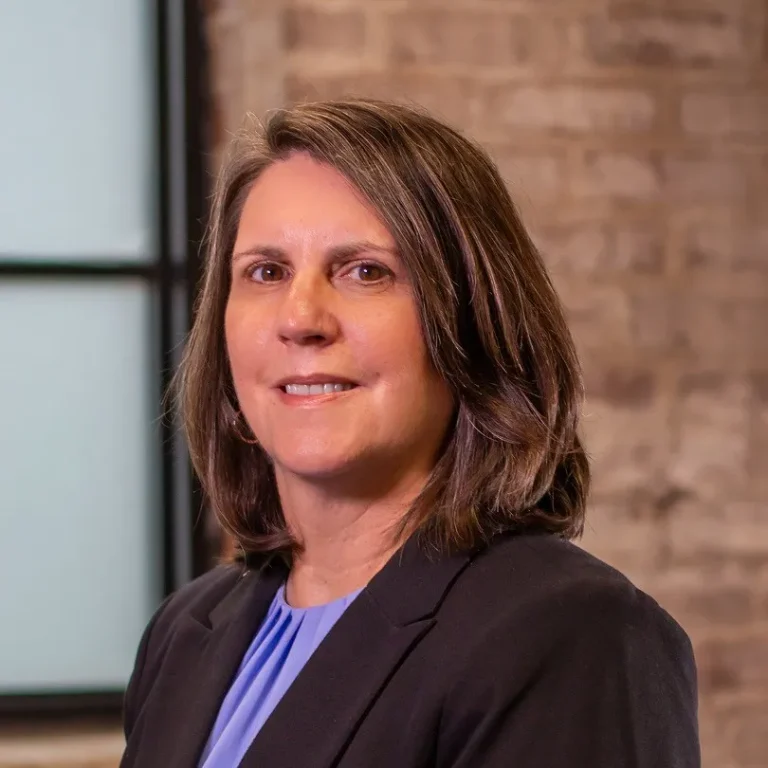 Woman in a blazer standing in front of a brick wall.