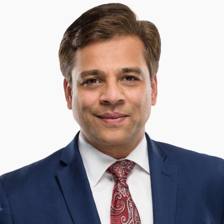Smiling man in a blue suit and red paisley tie on a white background.
