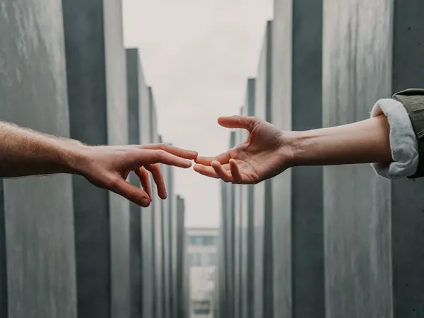 Two hands reaching towards each other between tall concrete structures.