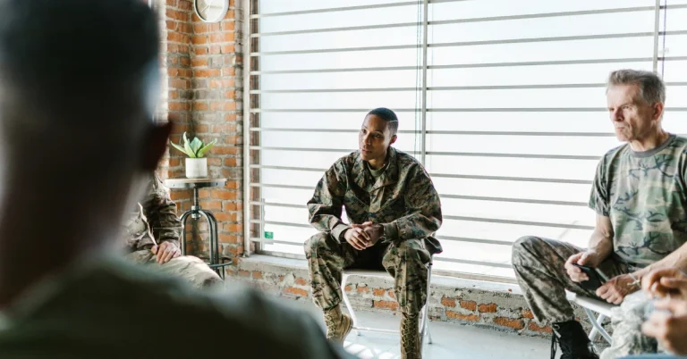 Military personnel sitting in a group circle during a discussion in a bright room.