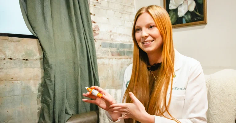 A smiling physician assistant in a white lab coat holding and explaining Spravato esketamine nasal spray to a patient during a mental health treatment consultation